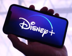 A hand holding a phone that has the Disney+ logo on it.