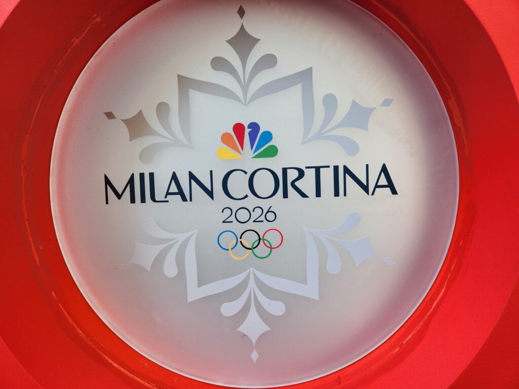 A promotional sign for the Milan Cortina Olympic Games 2026, featuring the NBC peacock logo.