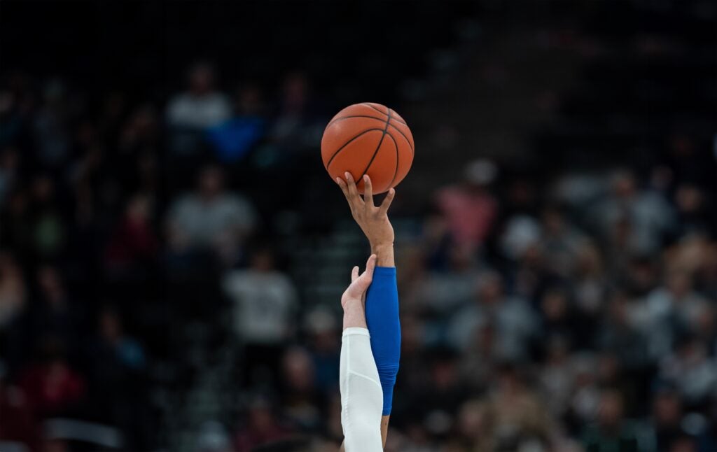 Two hands reaching up for a basketball in a crowded stadium