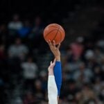 Two hands reaching up for a basketball in a crowded stadium